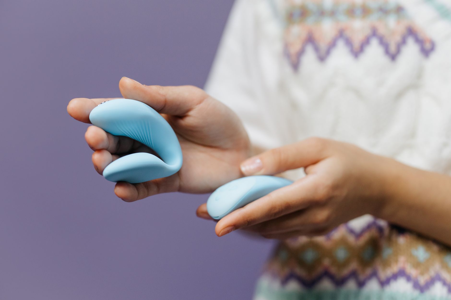Hand holding a sleek blue vibrator against a soft purple background, representing intimate reconnection